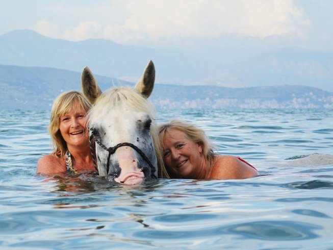 2 ladies swimming with a white horse